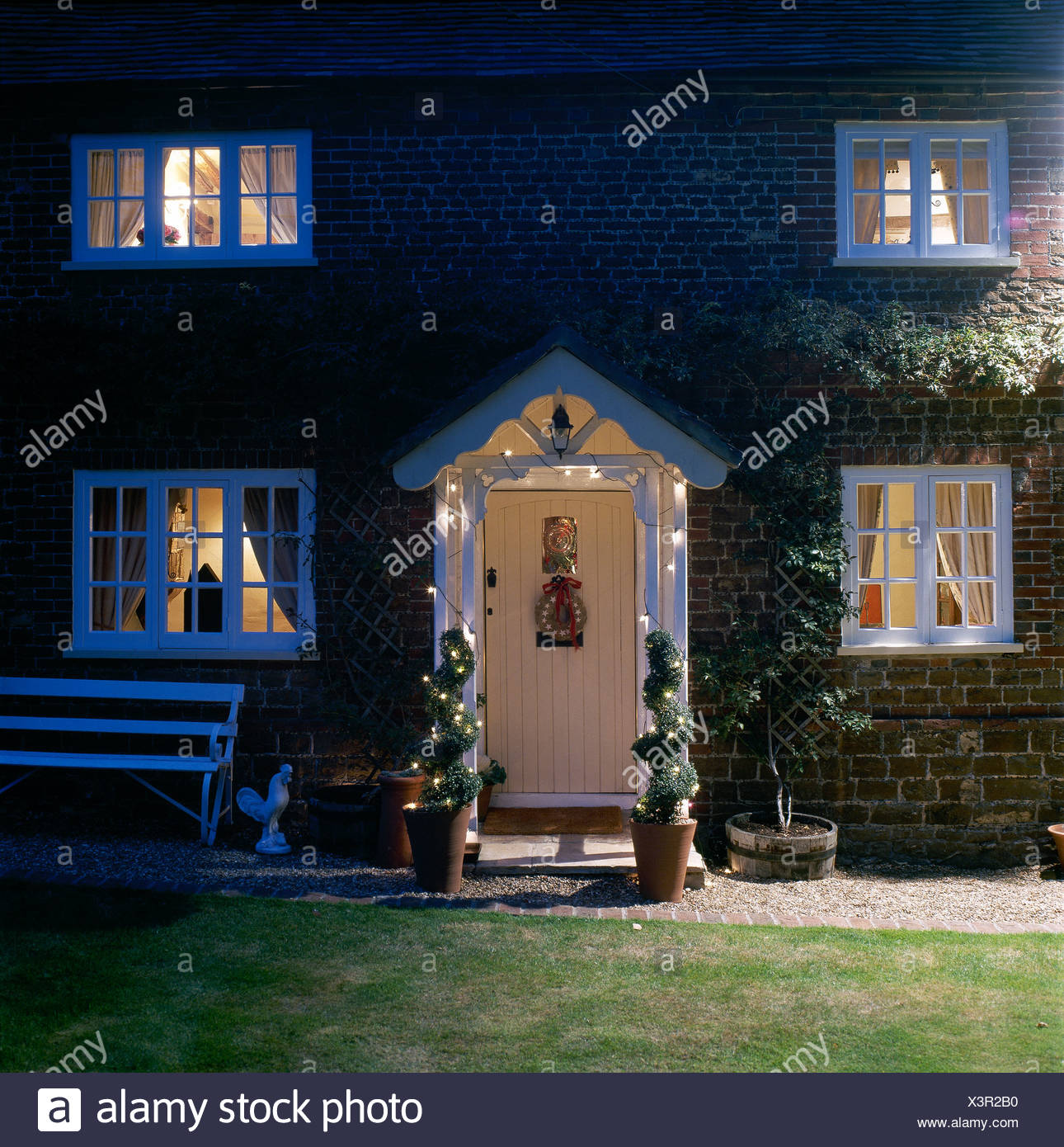Country Cottage Lit At Night And With Topiary Spirals In