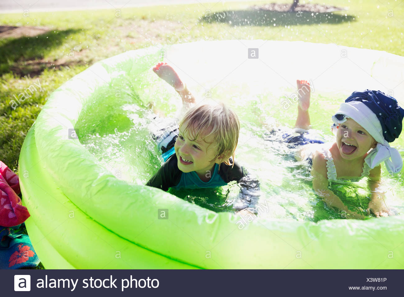Playful Brother And Sister In Wading Pool In Sunny Backyard Stock