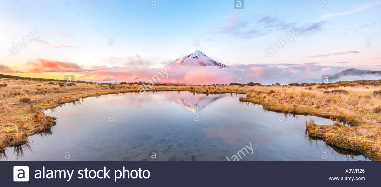 Reflection in Pouakai Tarn lake, pink clouds around stratovolcano Mount Taranaki or Mount Egmont at sunset, Egmont National Park Stock Photo