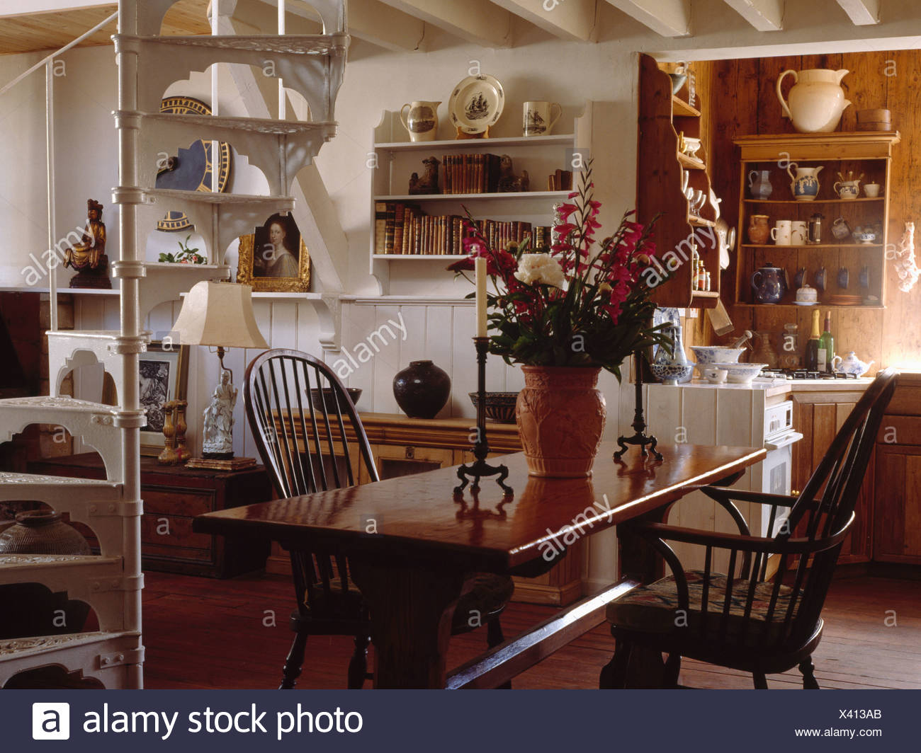 Polished Wood Table And Windsor Chairs In Small Cottage Dining Room With White Spiral Staircase And Wall Shelves Stock Photo Alamy
