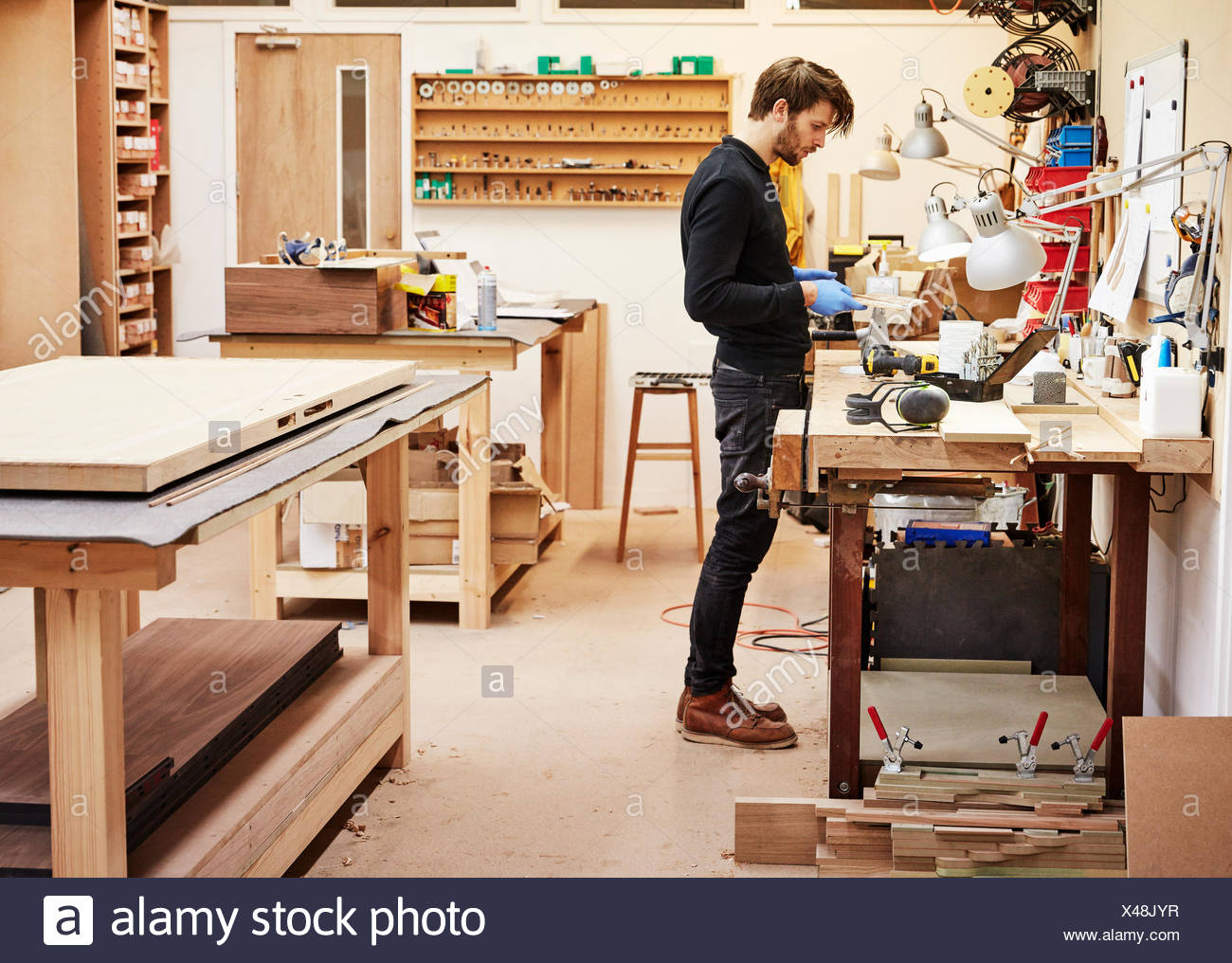 A Man Standing At A Workbench Holding And Examining An Object
