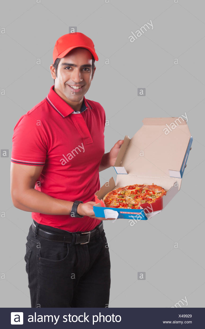 Portrait Of Smiling Delivery Man Showing Pizza Against Gray Background Stock Photo Alamy