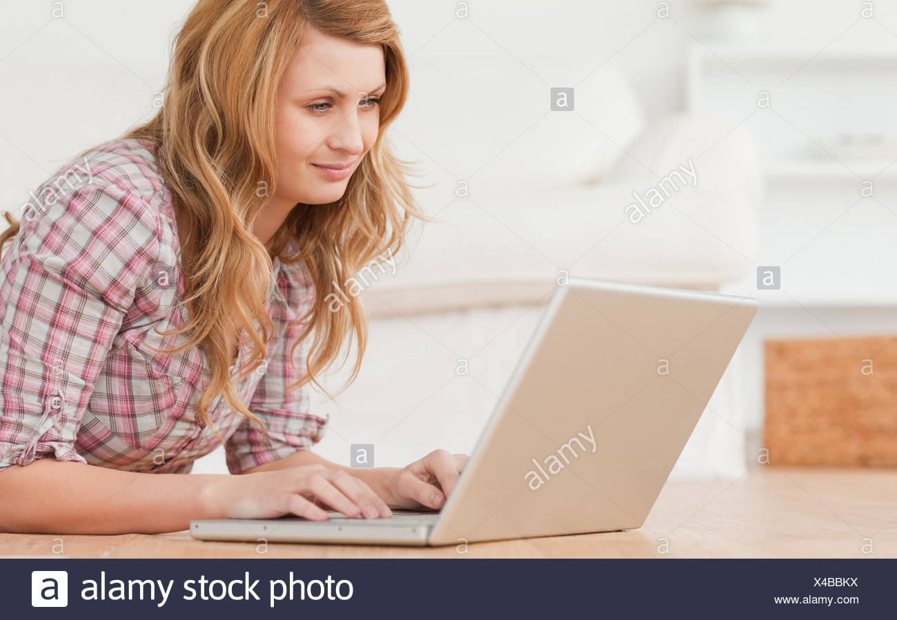 Blond-haired woman working on her laptop lying down on the floor Stock Photo