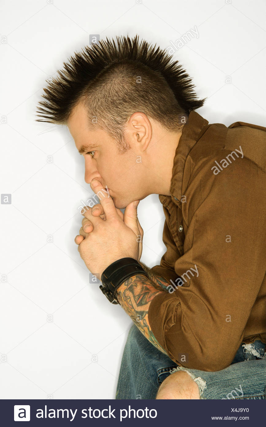 Side View Of Caucasian Man With Mohawk Sitting With Hands To
