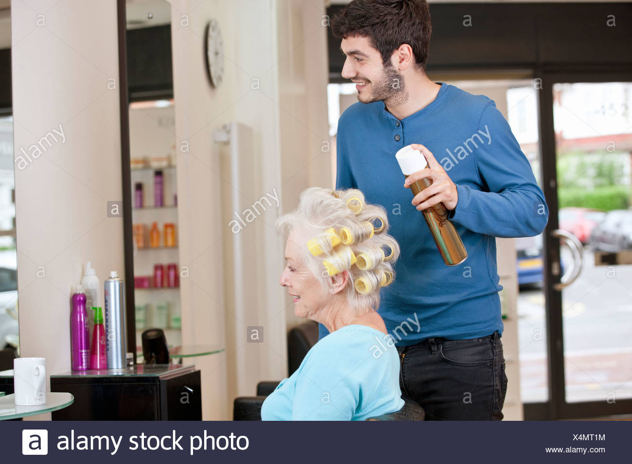 A Male Hairdresser Applying Hairspray To A Female Clients Hair