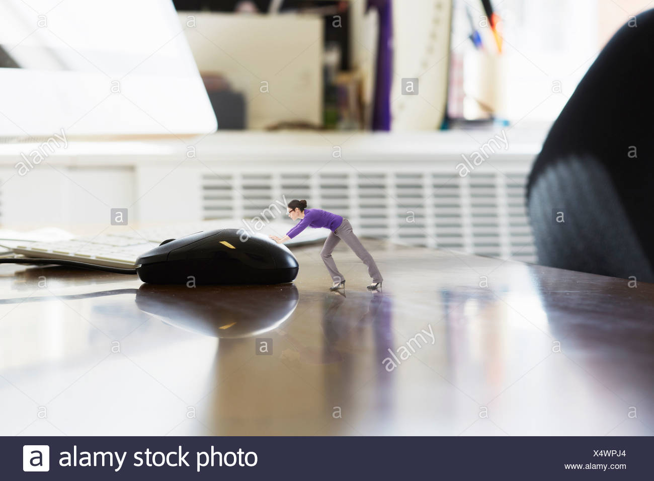 Businesswoman pushing large computer mouse on oversized desk Stock Photo