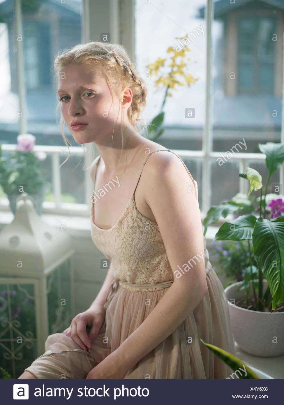 Young Woman With Blonde Plaited Hair In Room Filled With Plants