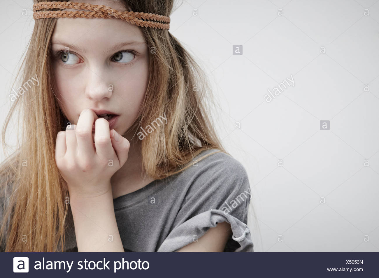 Portrait of girl wearing leather braid around head, holding feather, finger in mouth Stock Photo