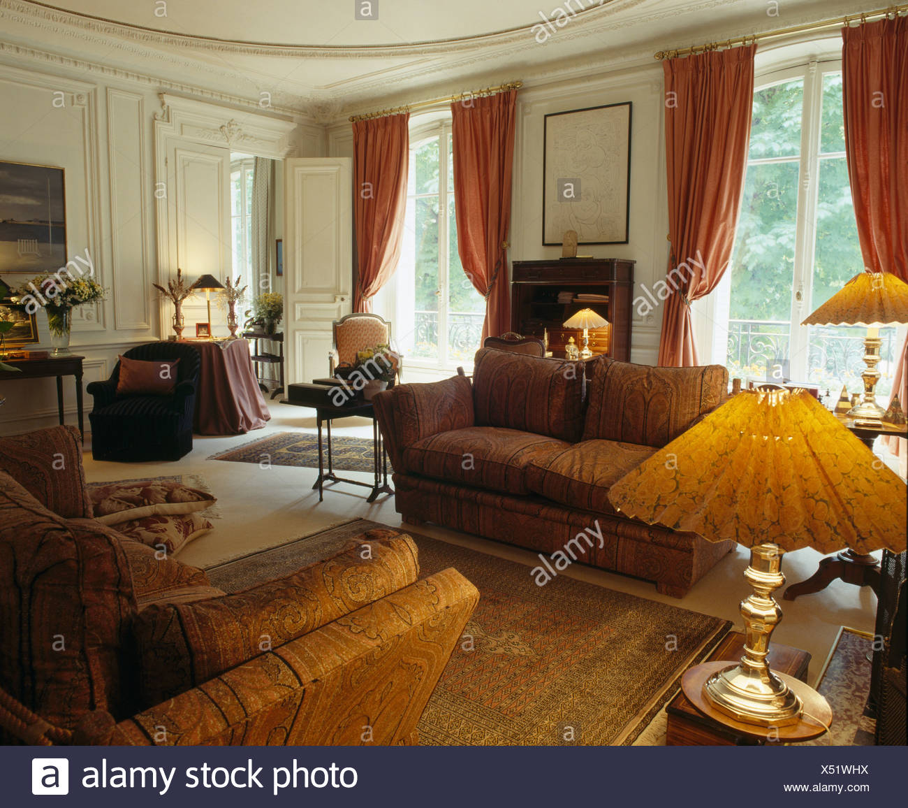 Lighted Lamps And Comfortable Brown Sofas In Country Drawing Room With Red Curtains At French Windows Stock Photo Alamy