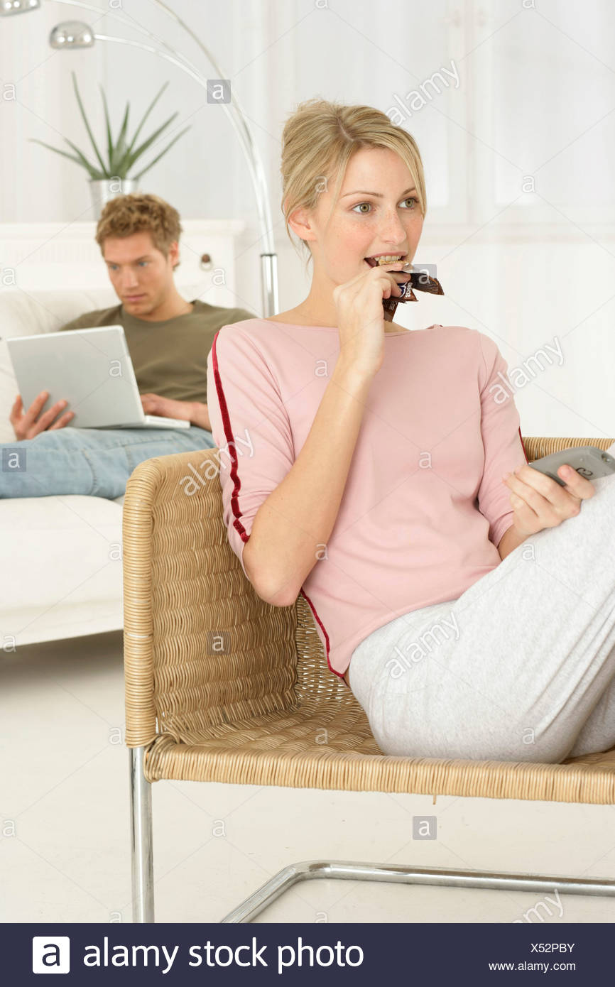 Woman Sitting On Chair Eating Candy Bar And Looking Tv Man