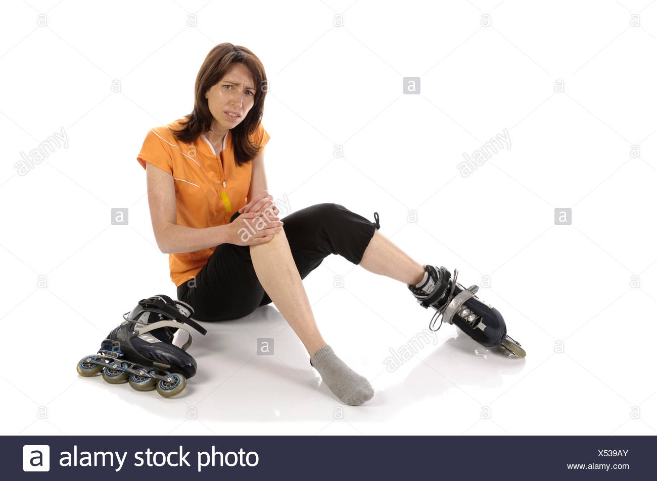 Erwachsene Sportlerin mit Inline-Skates hockt verletzt mit Schmerzen am Boden vor weißem Hintergrund. Stock Photo