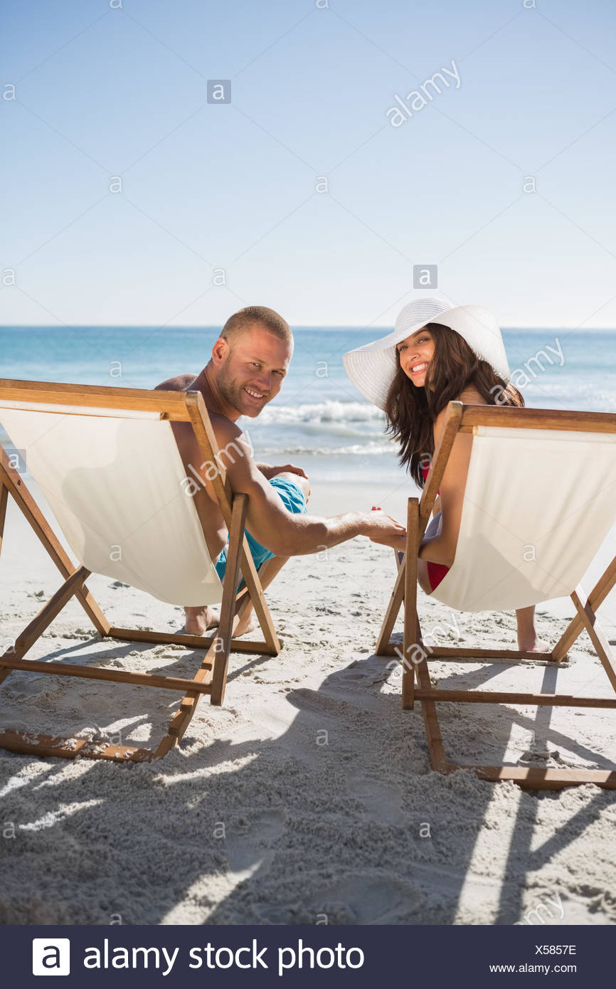 Cute Couple On The Beach Smiling At Camera While Lying On Their