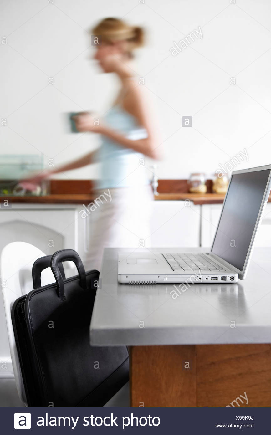 Woman In Kitchen Walking By Laptop Focus On Laptop Stock Photo