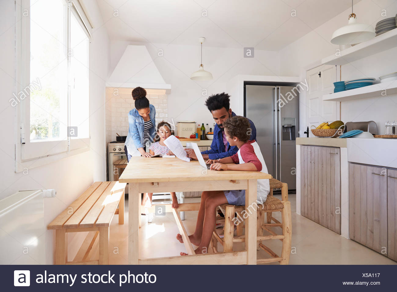 Mum And Dad Help Their Kids With Homework At Kitchen Table Stock