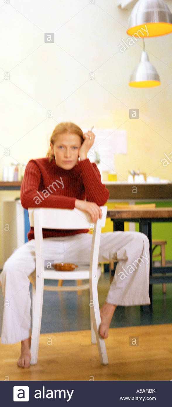 Young woman sitting backwards on chair smoking - Stock Image.