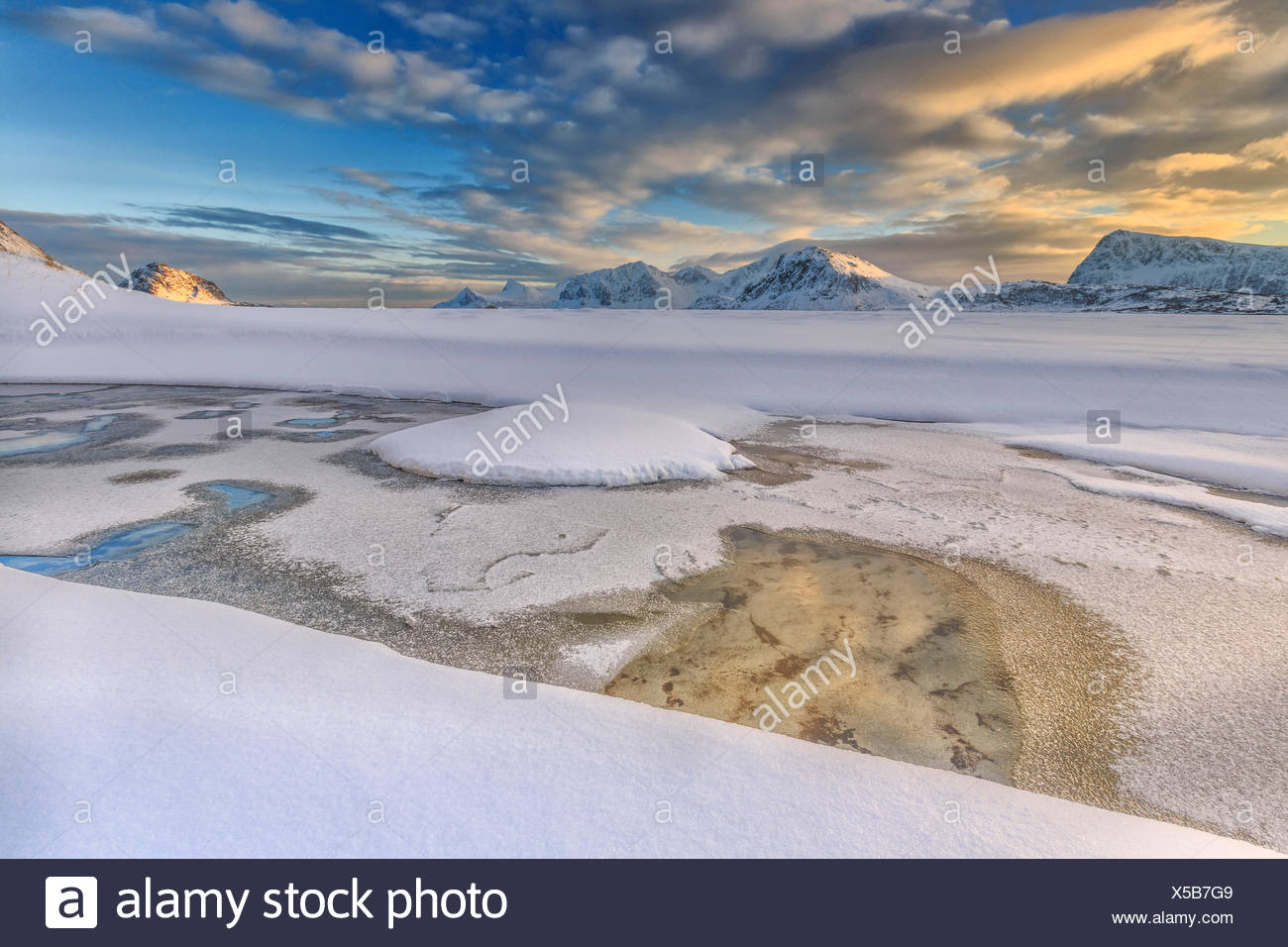 The golden sunrise reflected in a pool of the clear sea where the snow is almost melted. Haukland Lofoten Islands Norway Europe Stock Photo