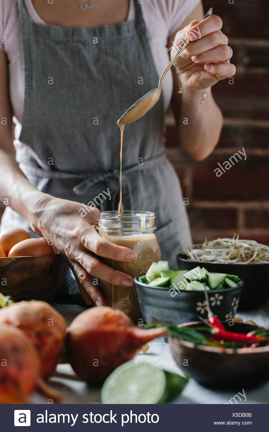 A woman is pouring warm peanut sauce into a jar. Stock Photo