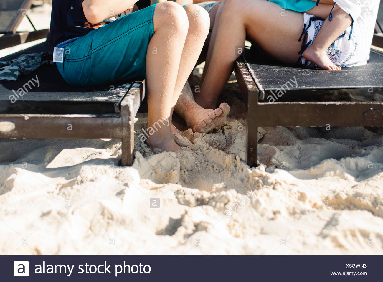 Mother and son sitting on sun loungers, mother holding young daughter, low section Stock Photo