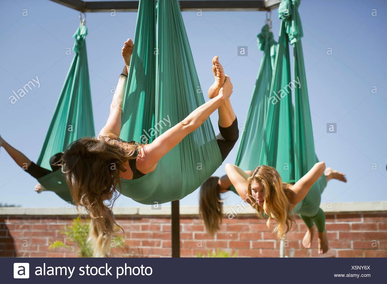 A woman takes bow pose while performing aerial yoga Stock Photo