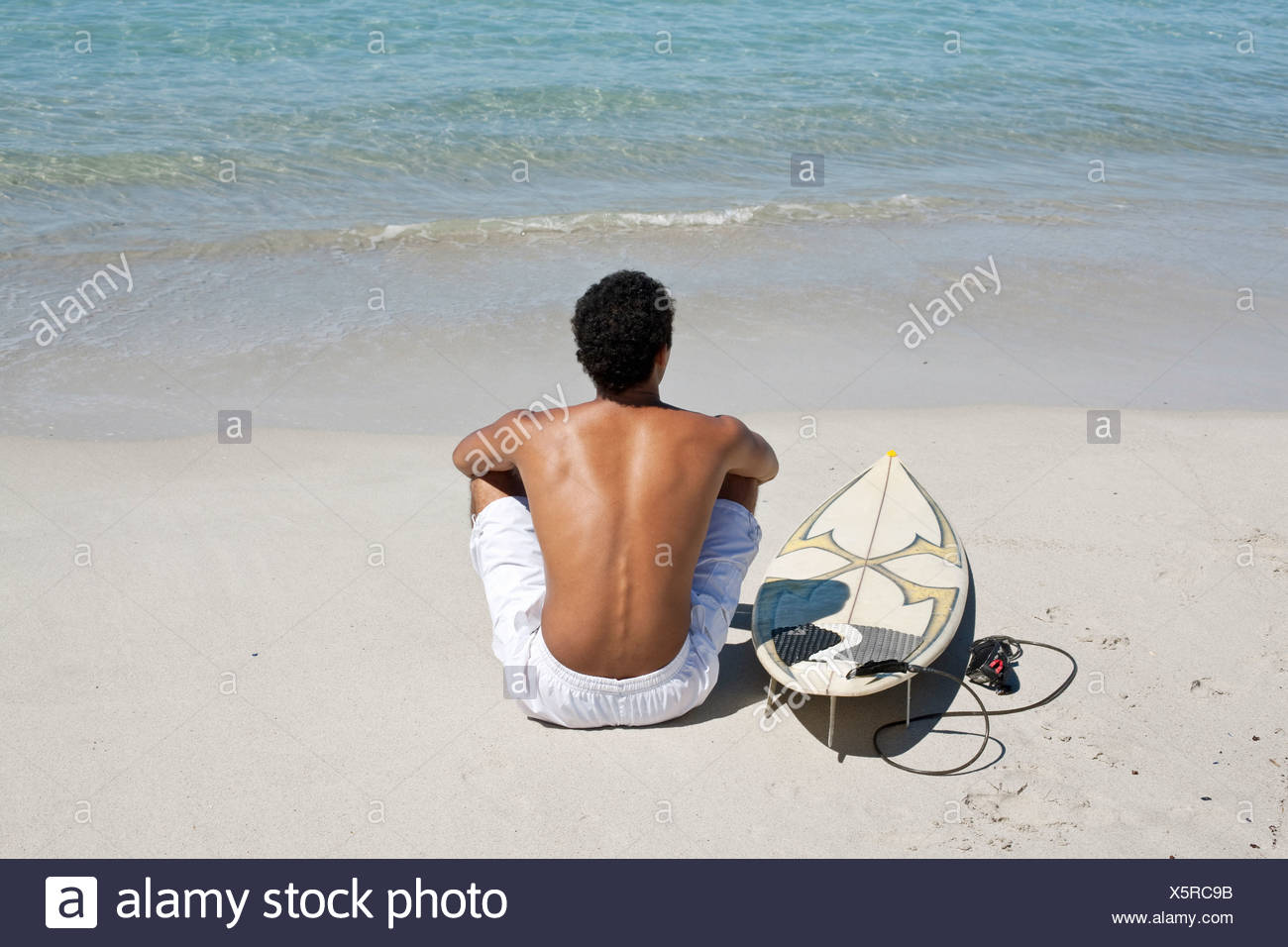 Rear View Of Young Man Sitting On Beach With Surfboard Stock Photo Alamy