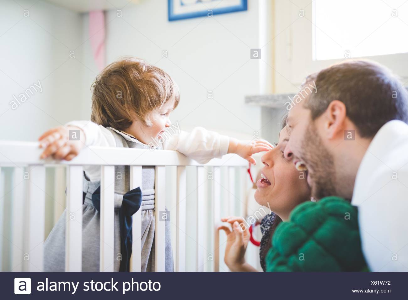 Mid Adult Couple Laughing With Toddler Daughter In Crib Stock