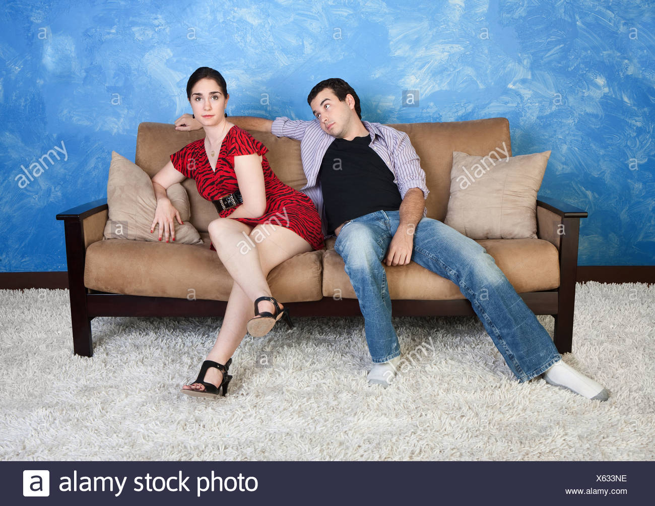 Annoyed Young Woman Sits On Sofa With Lazy Boyfriend Stock Photo