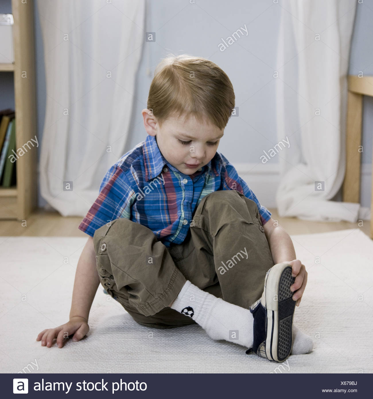 Young Boy Sitting On A Bench Putting On His Shoes At The 