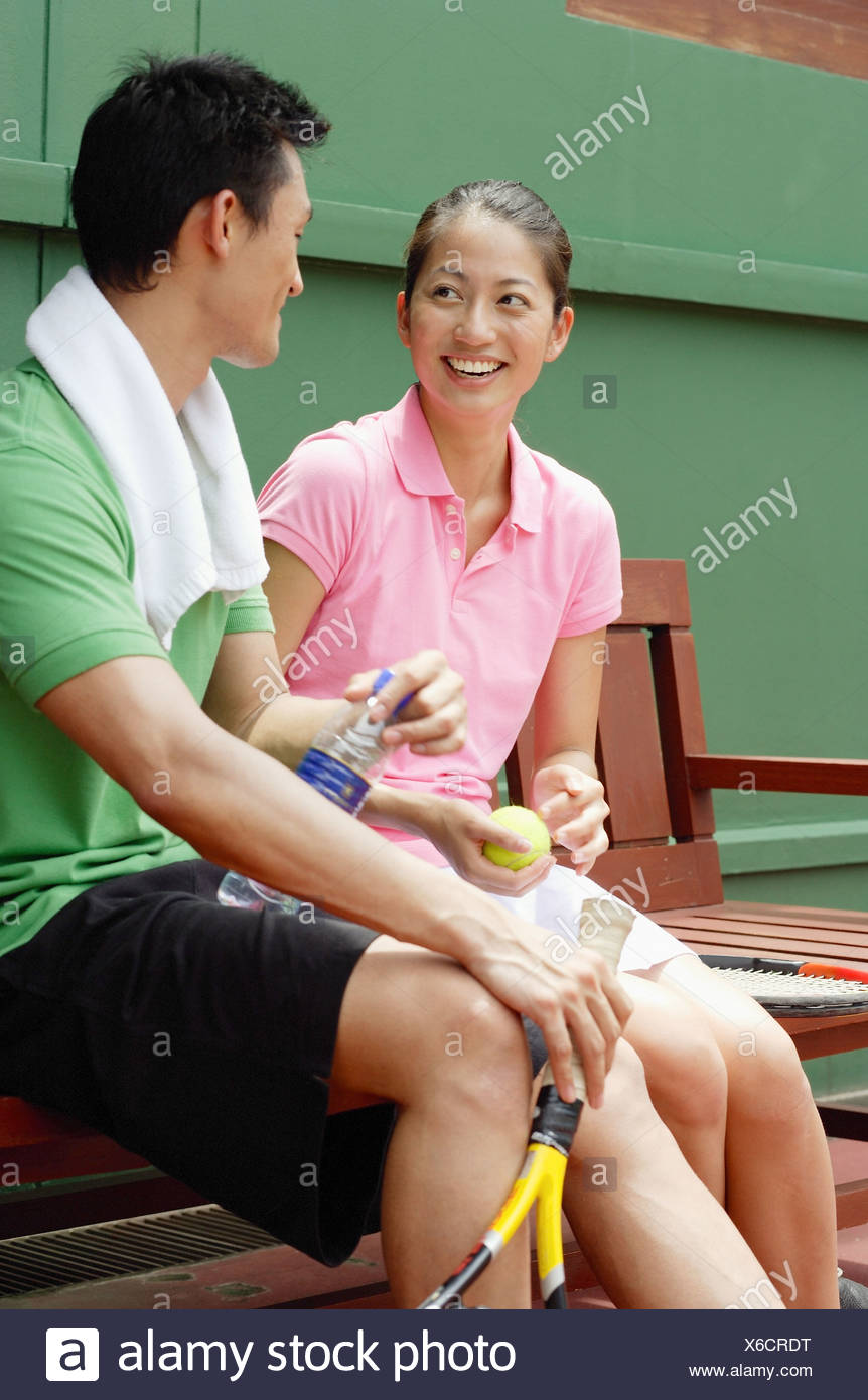 Couple Sitting On Bench In Tennis Court Looking At Each Other