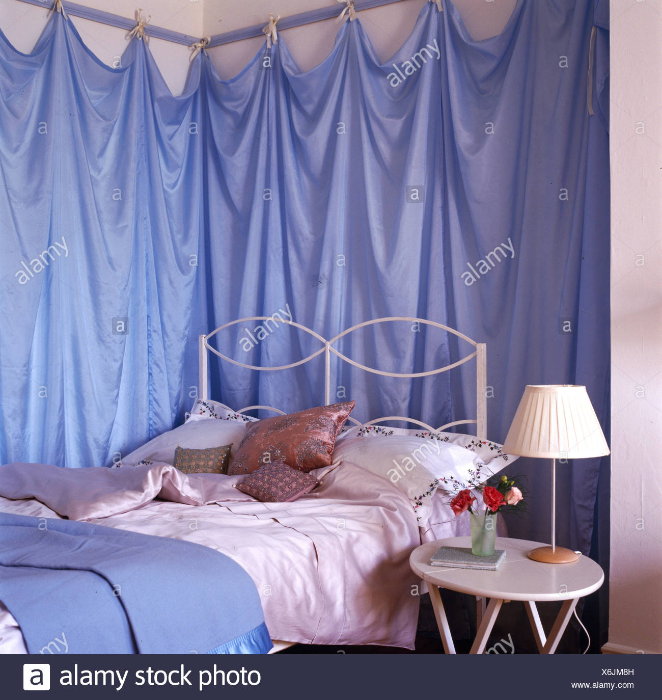 Corner Of Bedroom With Blue Fabric Drapes On Walls Above Bed Stock