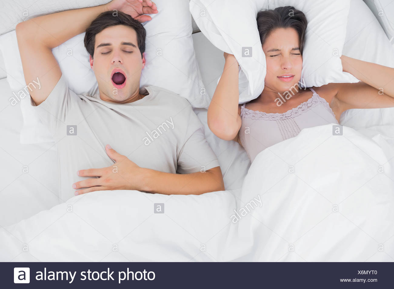 Woman Covering Ears With A Pillow While Her Partner Is Snoring