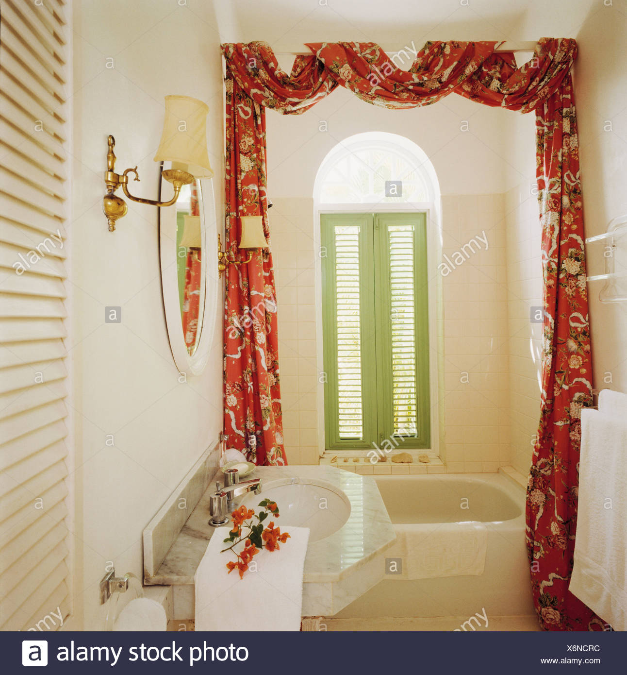 Green Shutters On Window Above Bath In Small White Bathroom With Patterned Red Drapes On Pole Above Bath Stock Photo Alamy