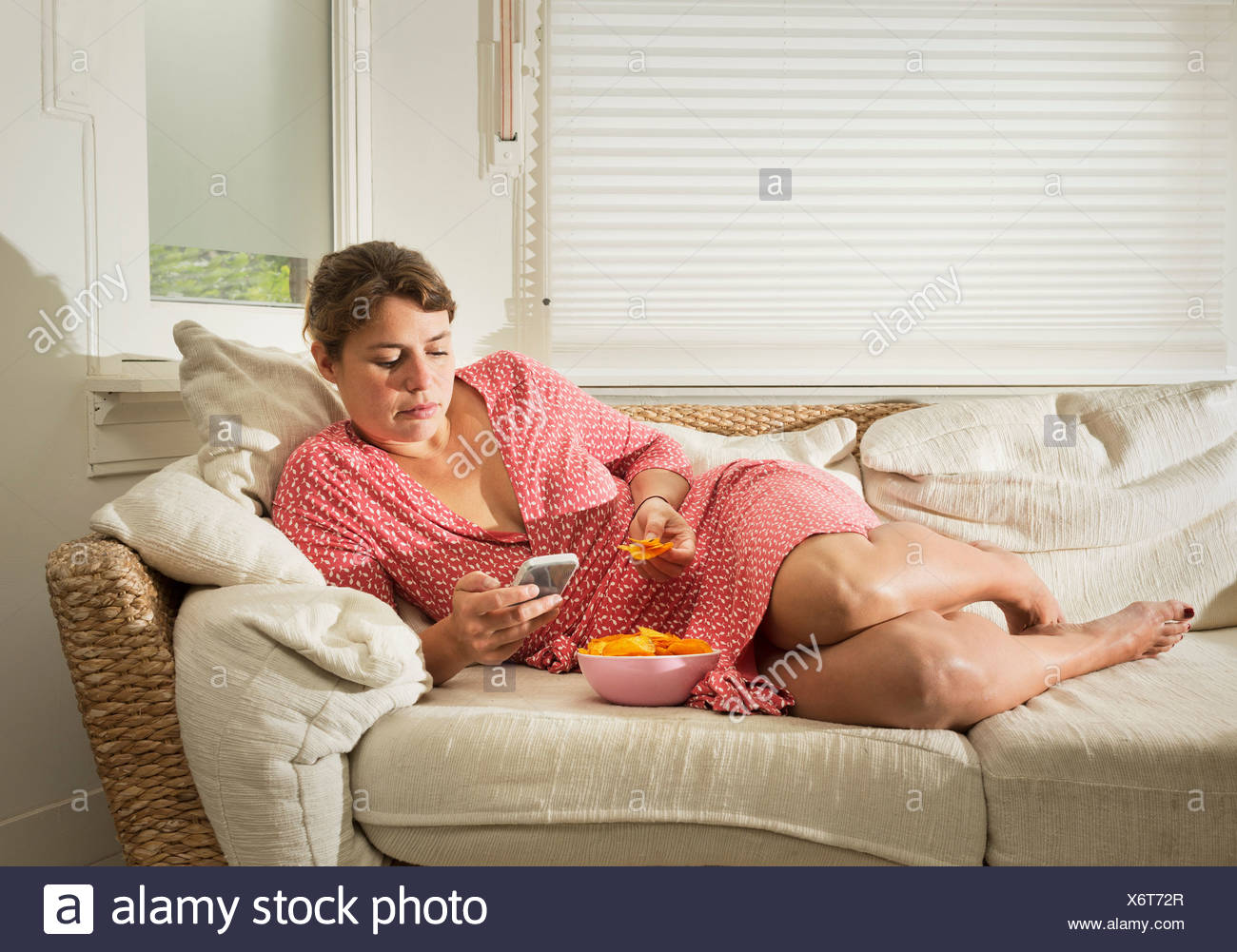 Woman Lying On Sofa Eating Bowl Of Crisps Stock Photo Alamy