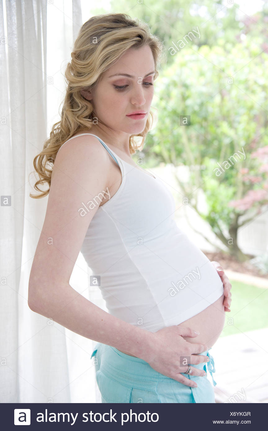 Pregnant Female Wavy Blonde Hair Wearing A White Vest And Blue