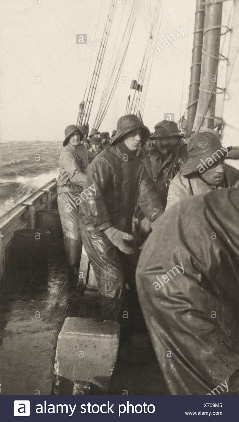 A group of fishermen, wearing rain gear, work on the deck of a ...