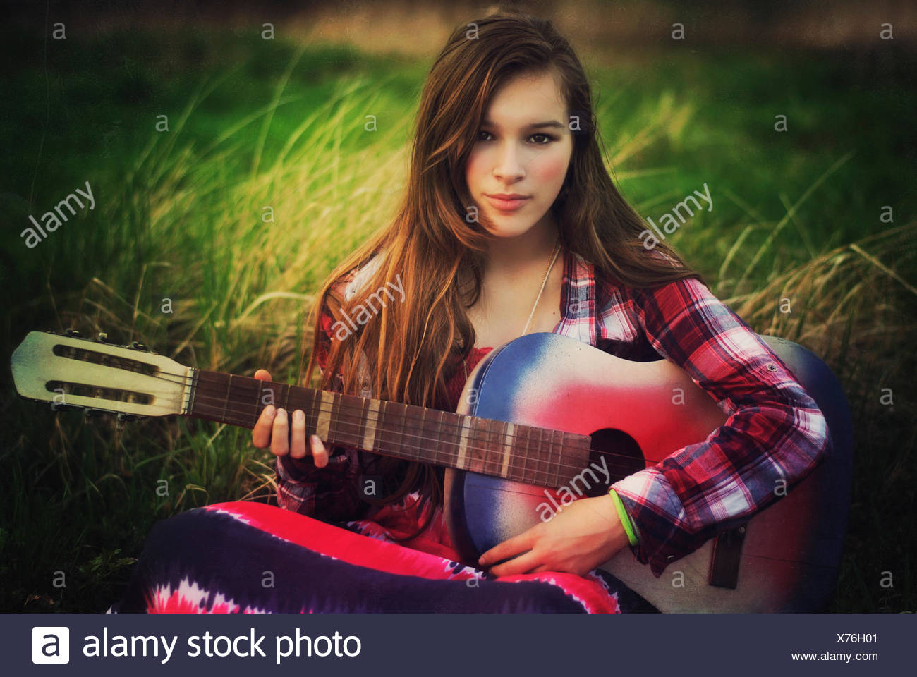 Portrait of a teenage girl sitting in a meadow with her guitar, Poland Stock Photo