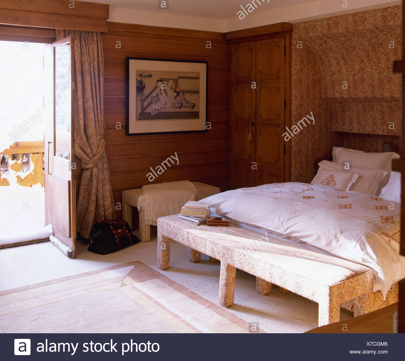 Upholstered Bench Seat Below Bed With Cream Duvet In Wood Paneled