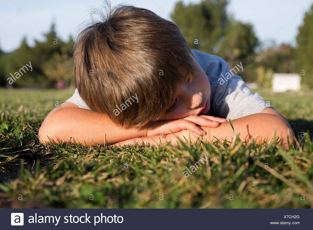 Sullen boy with head down lying on park grass Stock Photo
