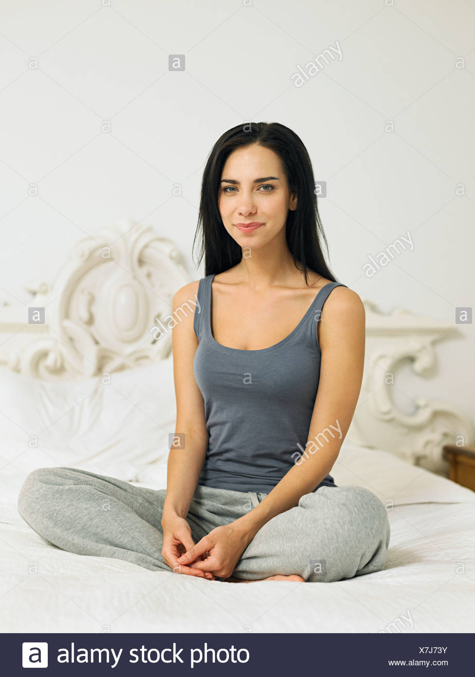 Young woman sitting cross legged on bed, portrait Stock Photo ...