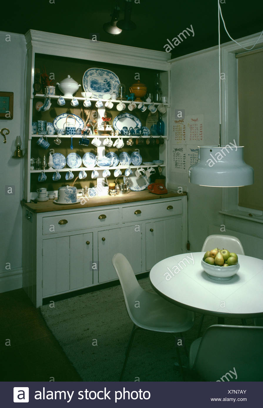 White Metal Pendant Light Above Modern White Circular Table And Chairs In Kitchen With White Plates On Painted White Dresser Stock Photo Alamy