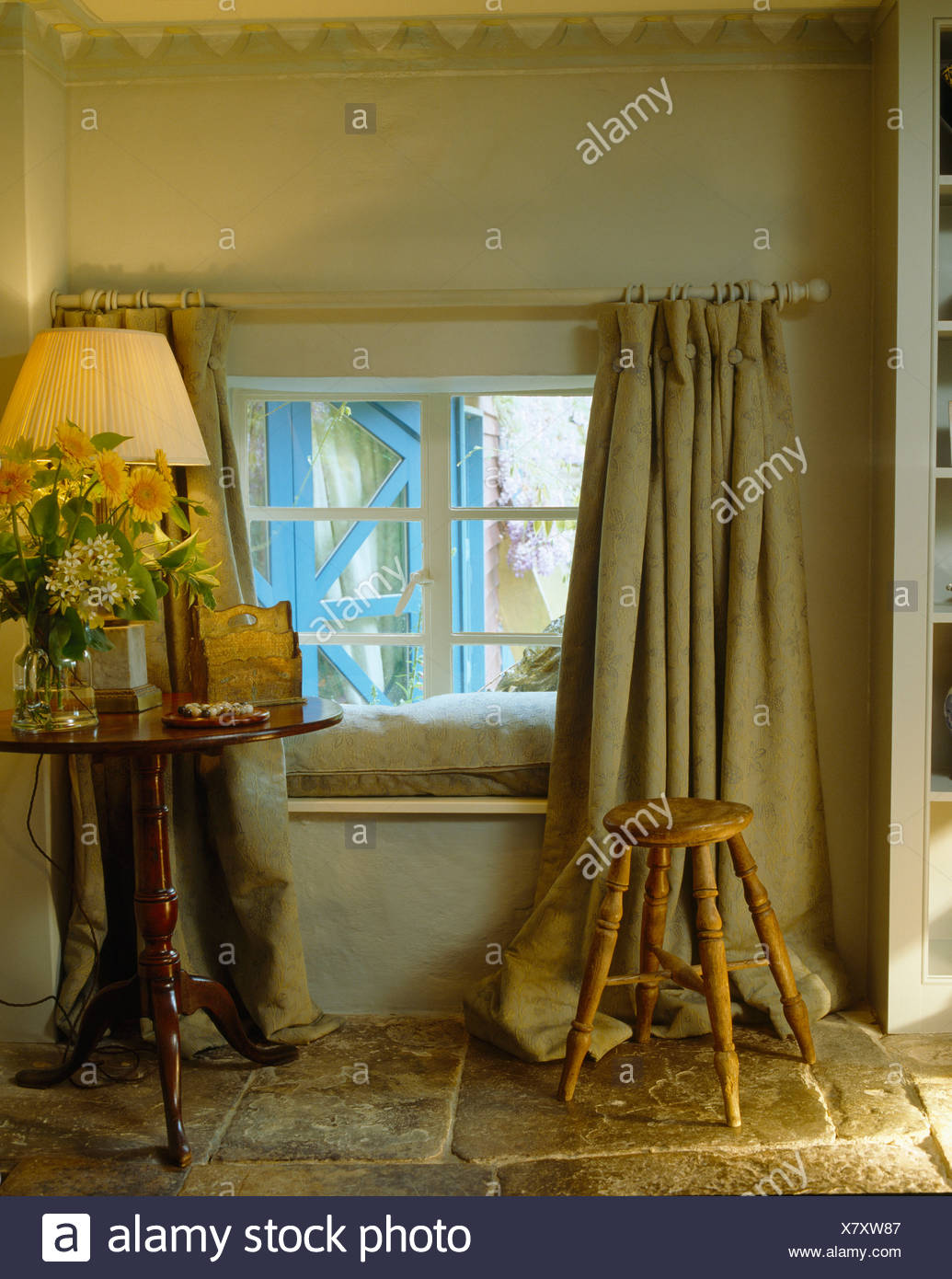 Lighted Lamp On Small Antique Table Beside Window With Heavy Linen