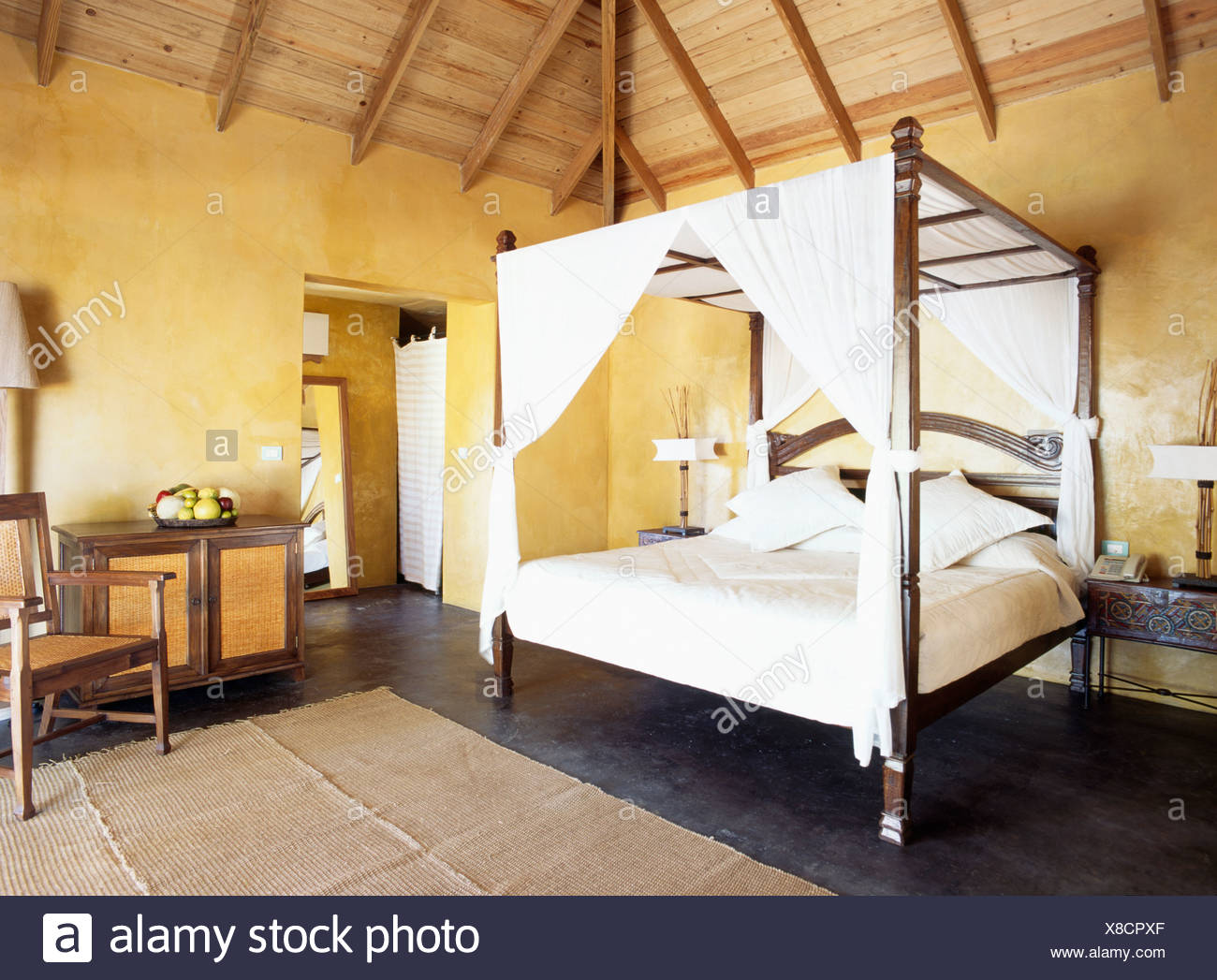 White Drapes And Bedlinen On Bed In Yellow Caribbean Bedroom Stock
