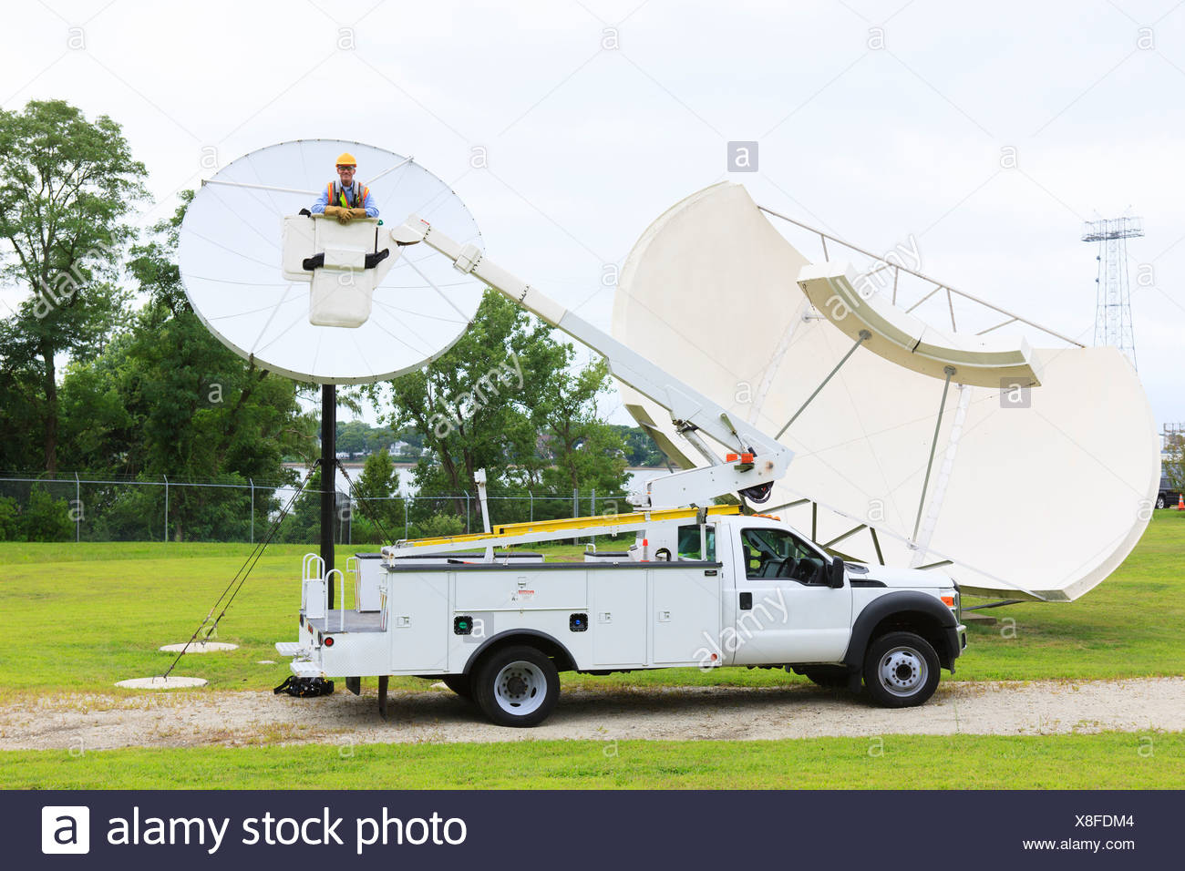 Communications engineer in bucket truck in front of satellite dish Communications engineer in bucket truck in front of satellite dish