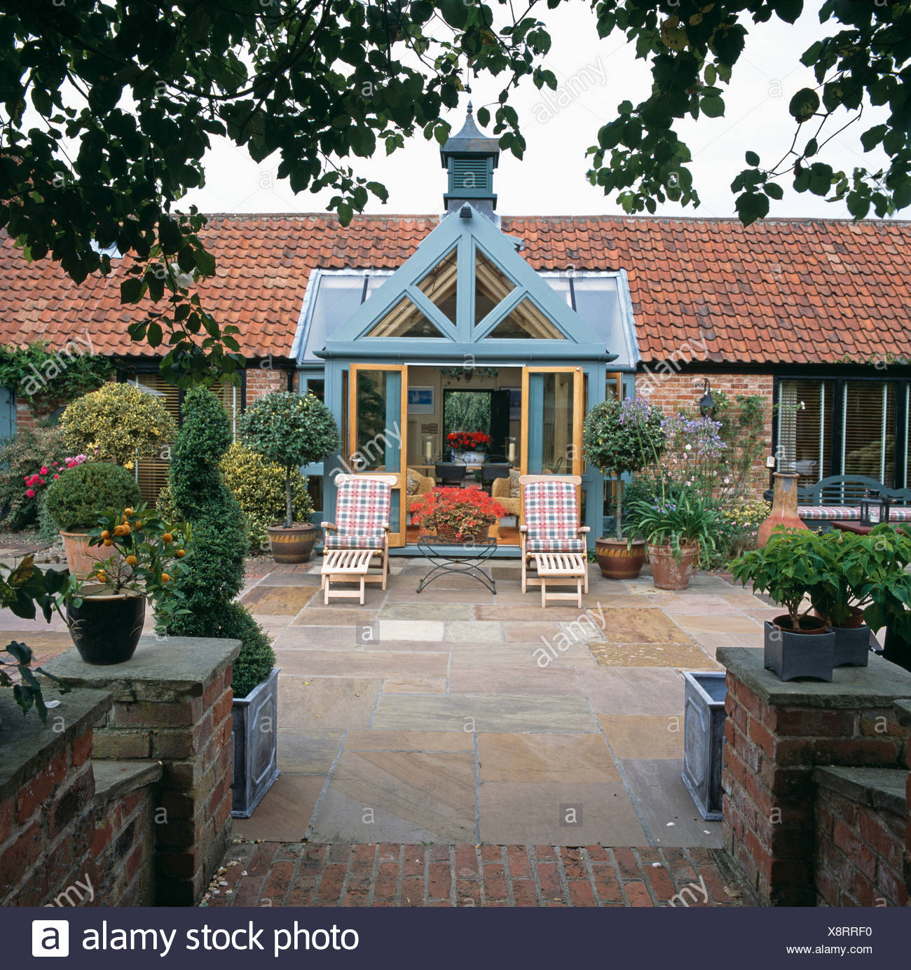 Barn Conversion Home With Paved Patio With Clipped Trees In Pots