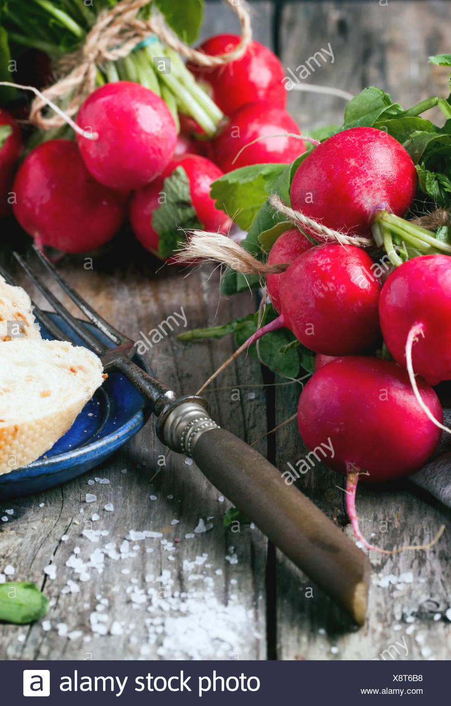Fresh wet radishes with vintage fork, sea salt and bread over old wooden table Stock Photo