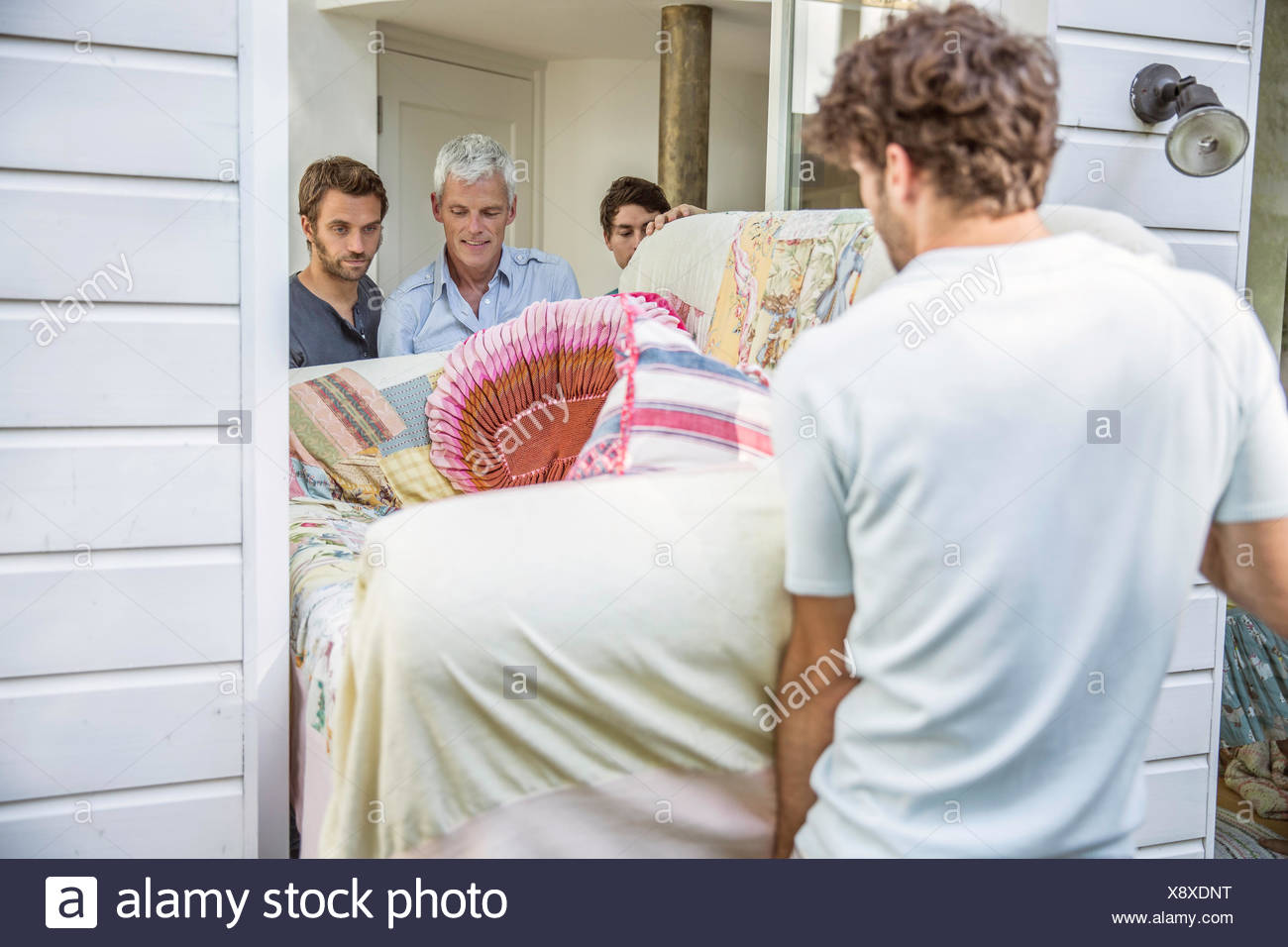 Male Adult Friends Moving Sofa Through Front Door Stock