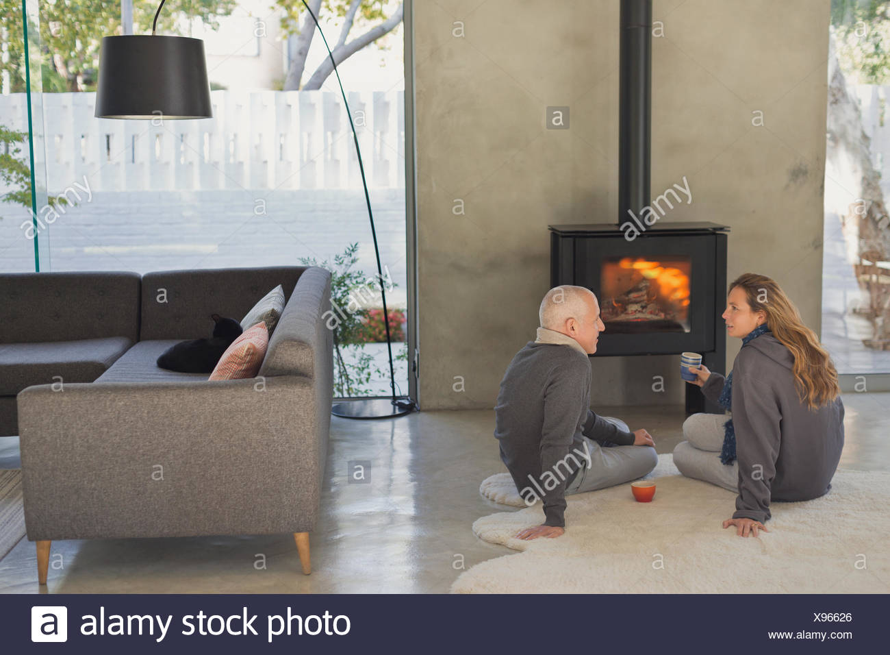 Couple Drinking Tea And Talking In Front Of Wood Stove Fireplace