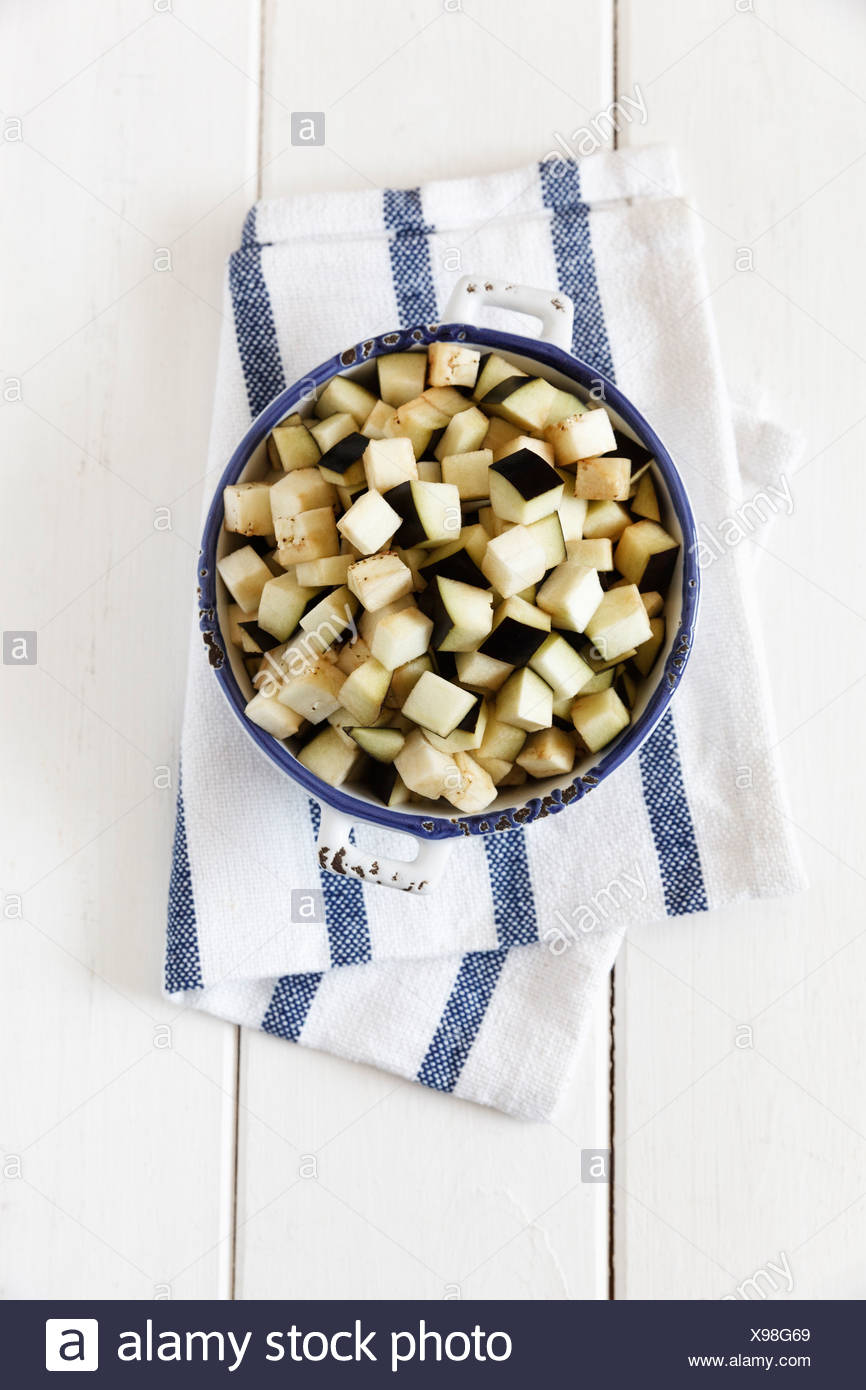 Bowl Of Diced Aubergine On Kitchen Towel And White Wood Stock