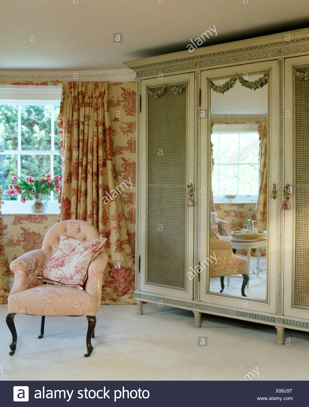 Pink armchair beside antique wardrobe with mirrored door in 