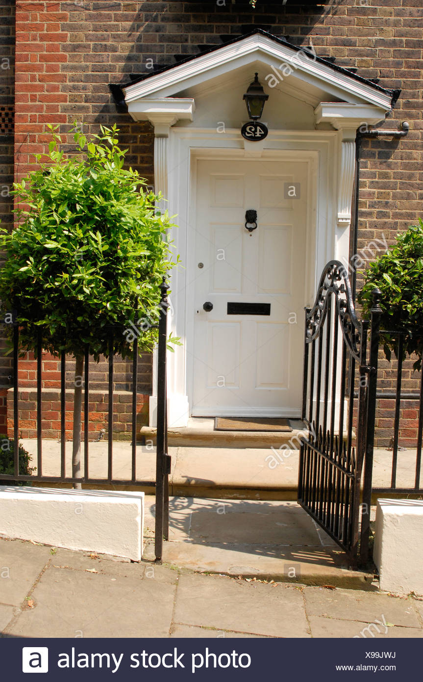 A White Front Dowith Pediment Black Railings And A Gate And