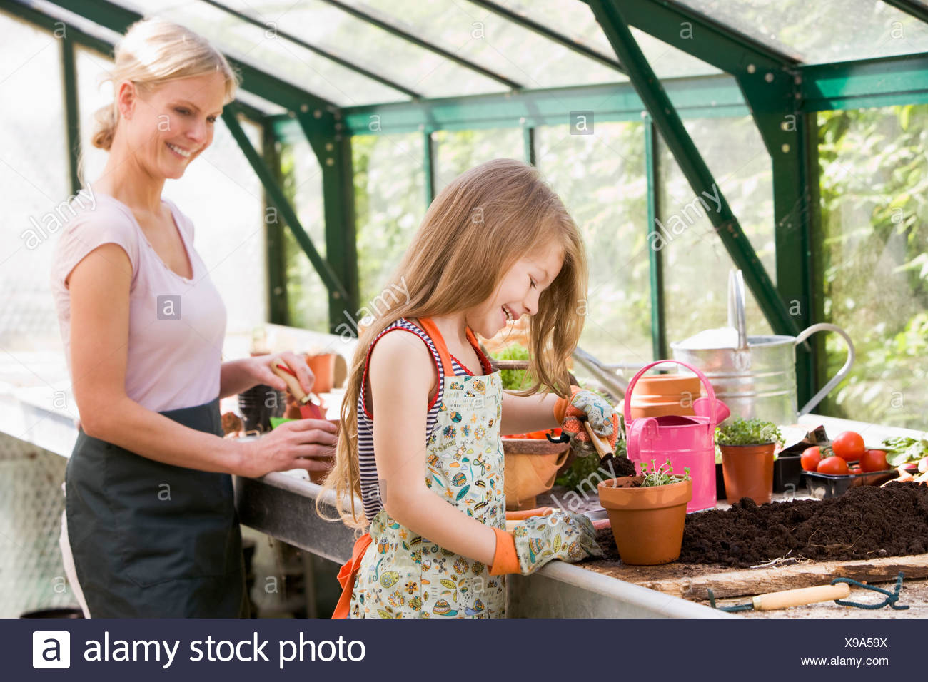 Young girl and woman in greenhouse putting soil in pots smiling Stock Photo